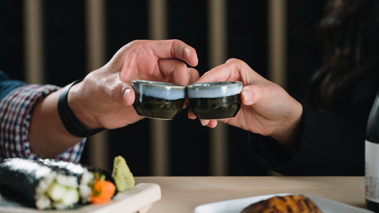 Two People Cheering Sake Cups While Dining